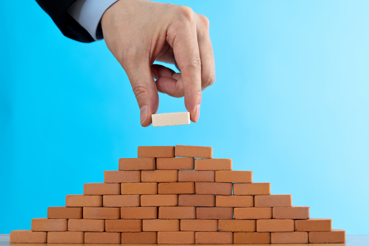 A person placing a brick on a pyramid, symbolizing the building blocks of technical data quality through accuracy, completeness, and consistency.